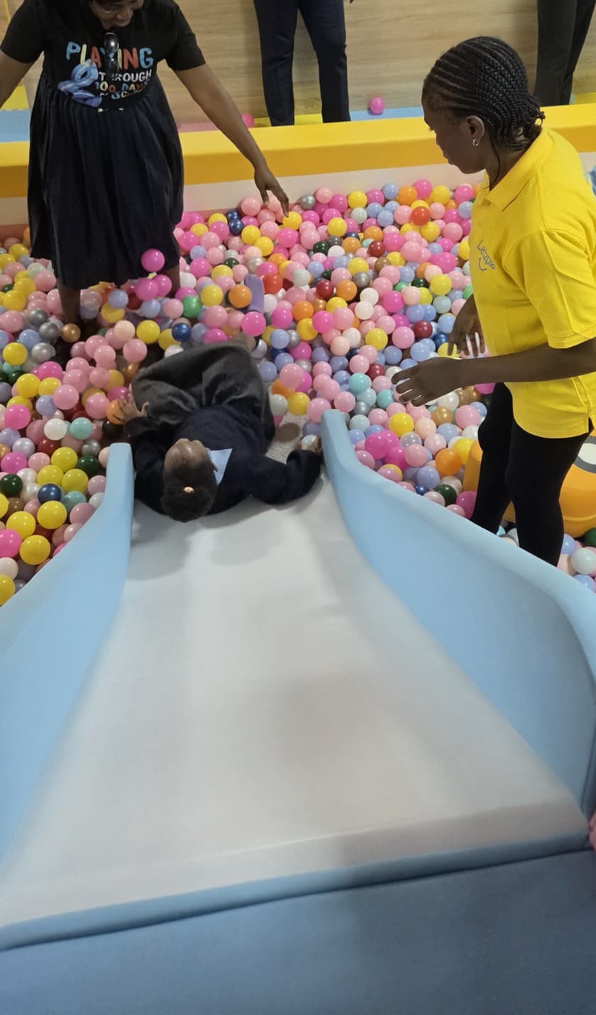 A child sliding into the ball pit while a Letzplay staff member in a yellow polo shirt supervises close by.
